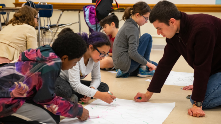 Worlds of Connections undergraduate mentor Luke Novak (right) works with a group of middle-school students to play a game demonstrating network science and the efficacy of vaccinations among community members.